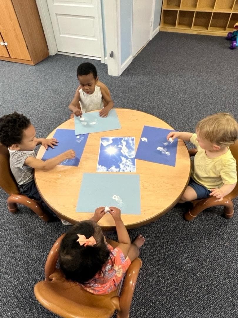 Toddlers making cloud pictures with cotton balls at a round table