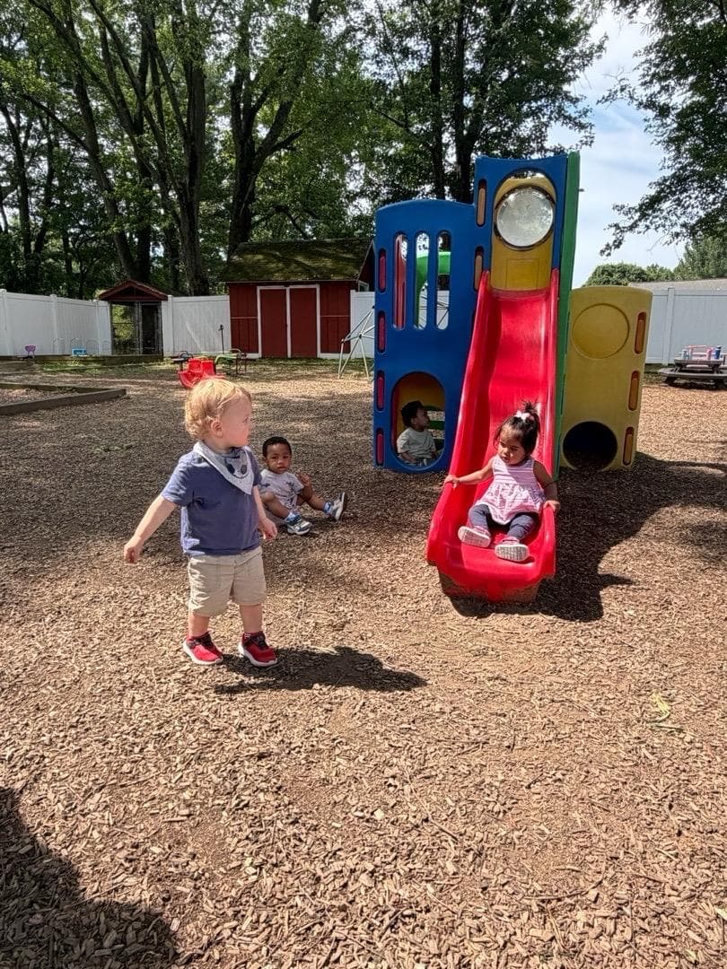 A toddler going down the red slide on the playground