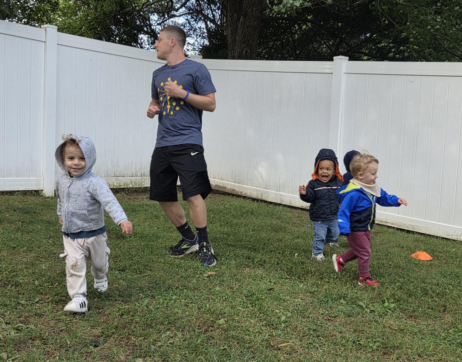 Toddlers running and laughing on the grass with a coach