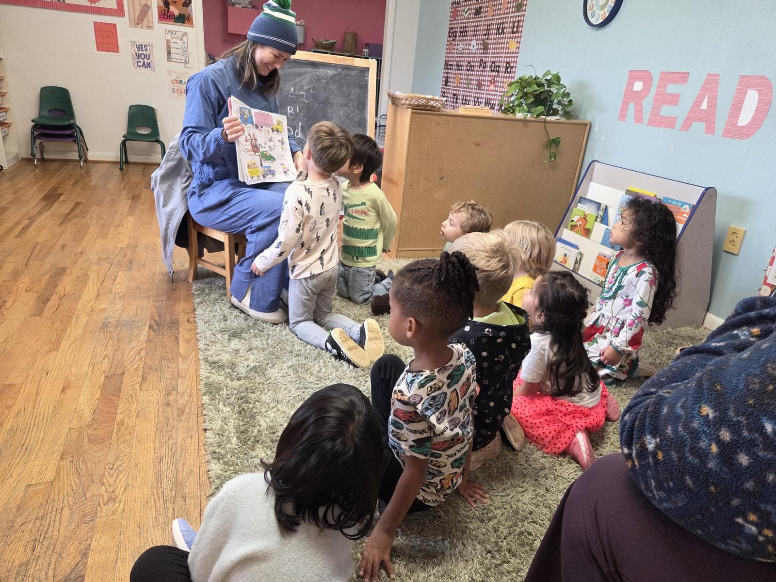 A teacher reading a picture book to preschoolers gathered on the rug